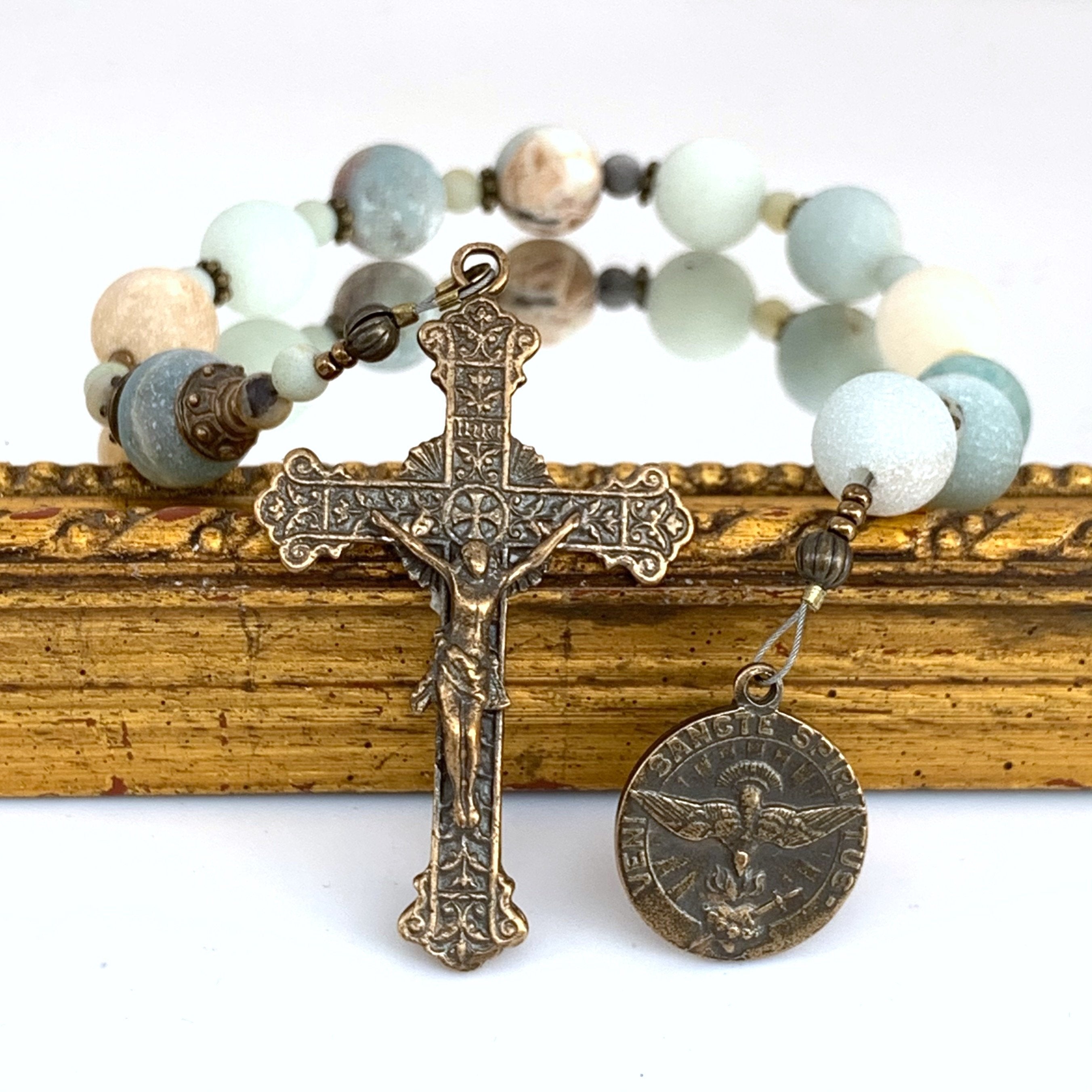 Rosary with Holy Spirit bronze medal on right, Sacred heart crucifix on left with Amazonite Ave Maria beads in background.
