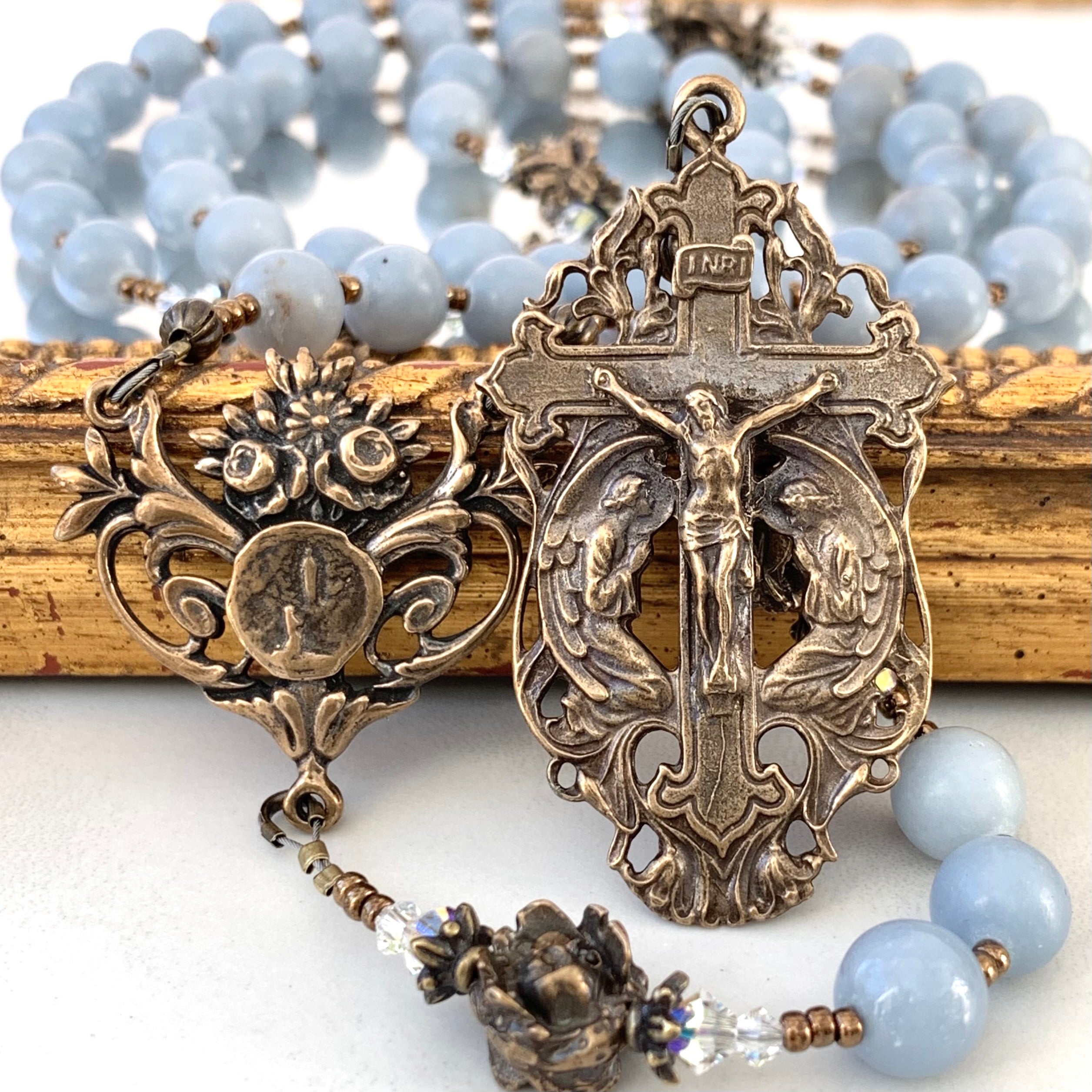 Close up view of angels kneeling crucifix, Lourdes center and angel stone rosary beads in the backgorund.