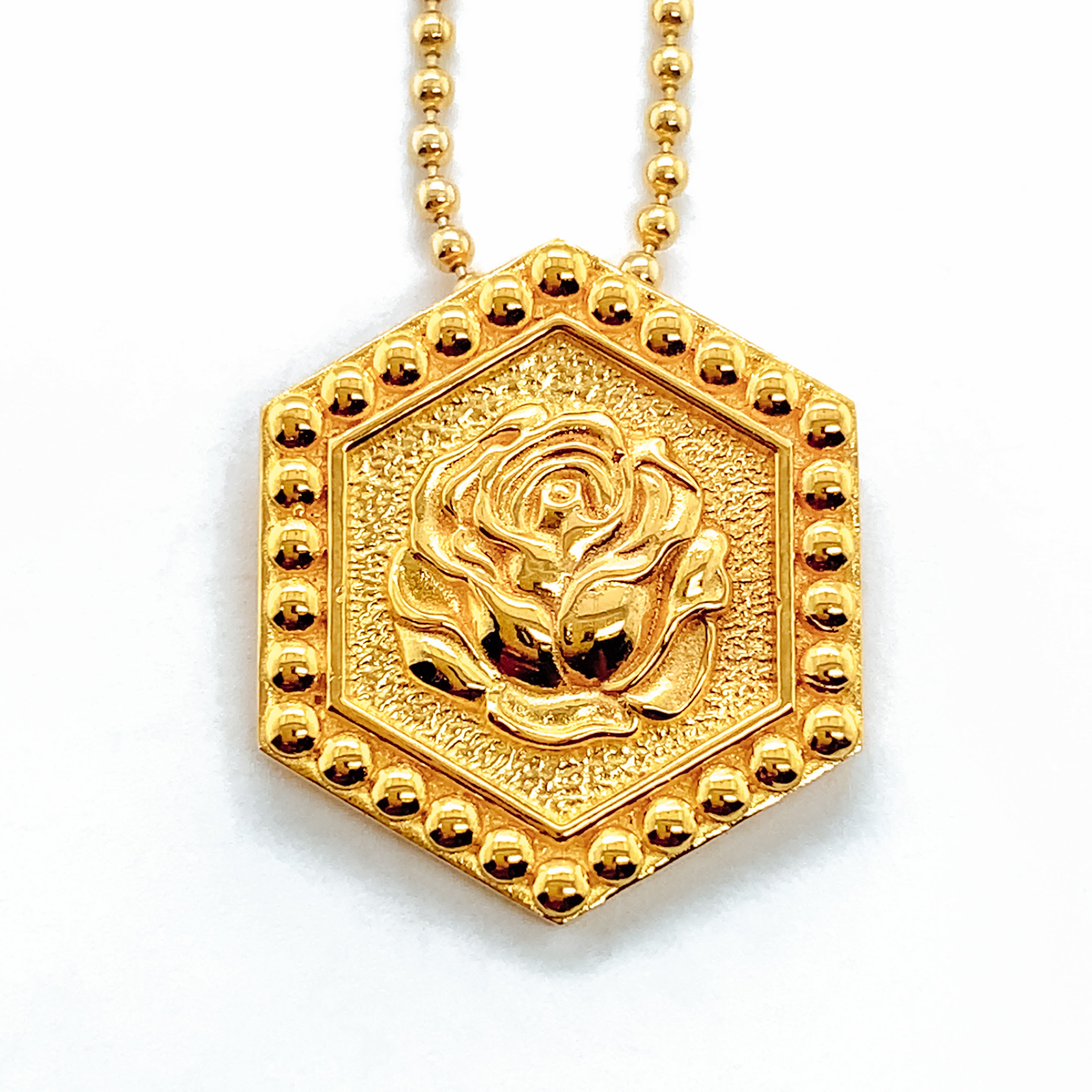 Gold hexagonal pendant hung on a bead chain. The pendant features a rose in the center, and raised dots around the border.
