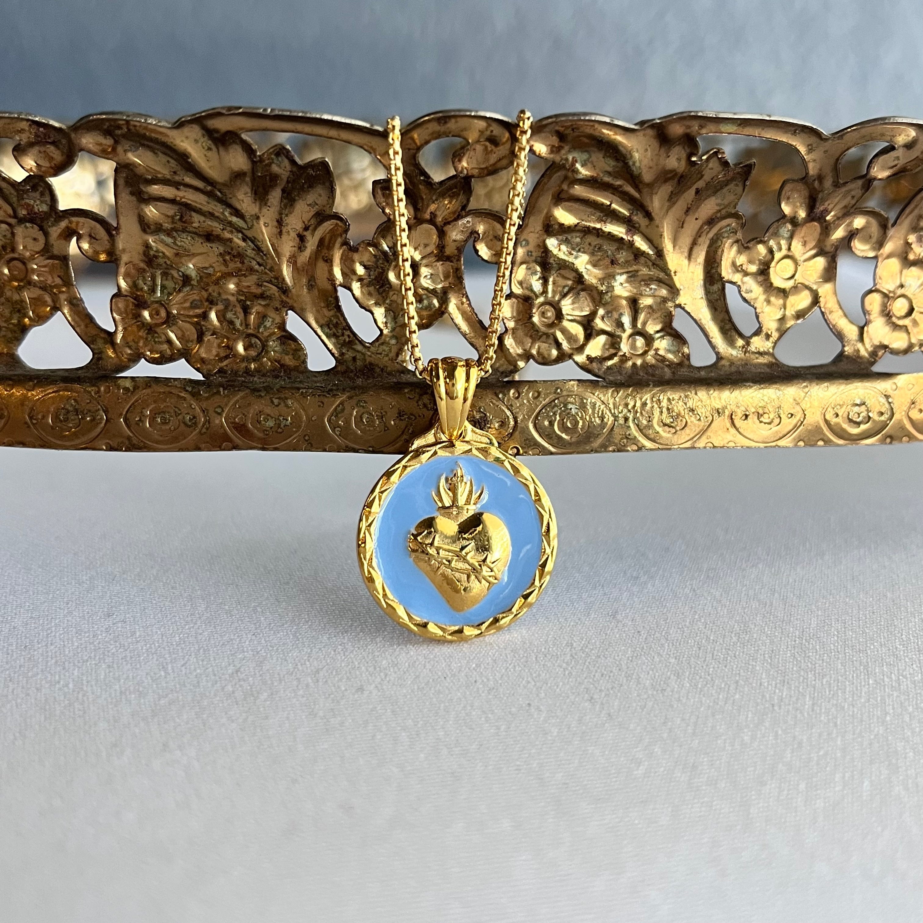 High end Catholic Jewelry Gold necklace featuring a sacred heart pendant on a decorative table against a gray background
