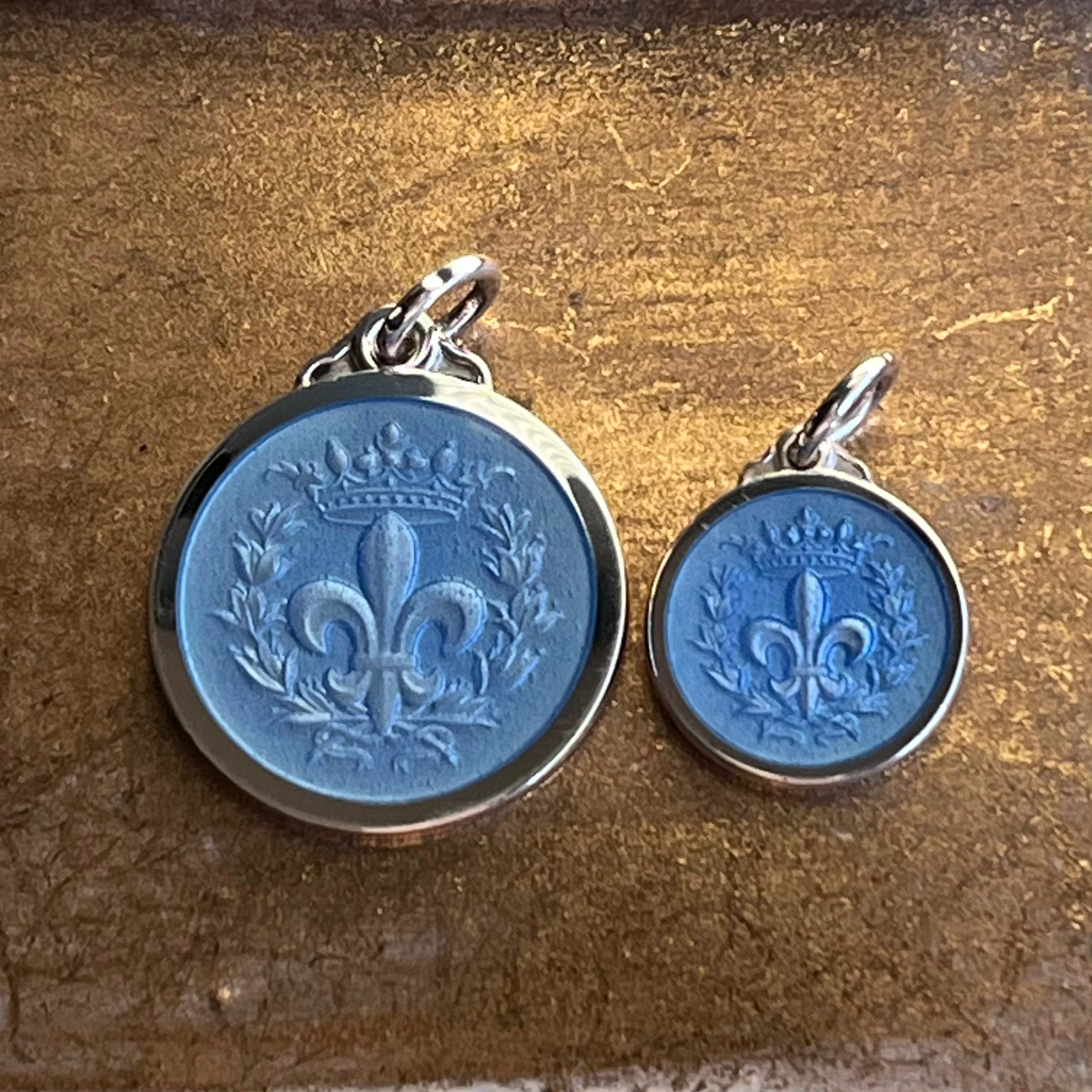 Showing two sizes of sterling silver french blue fleur de lis necklace pendants overlain with translucent enamel