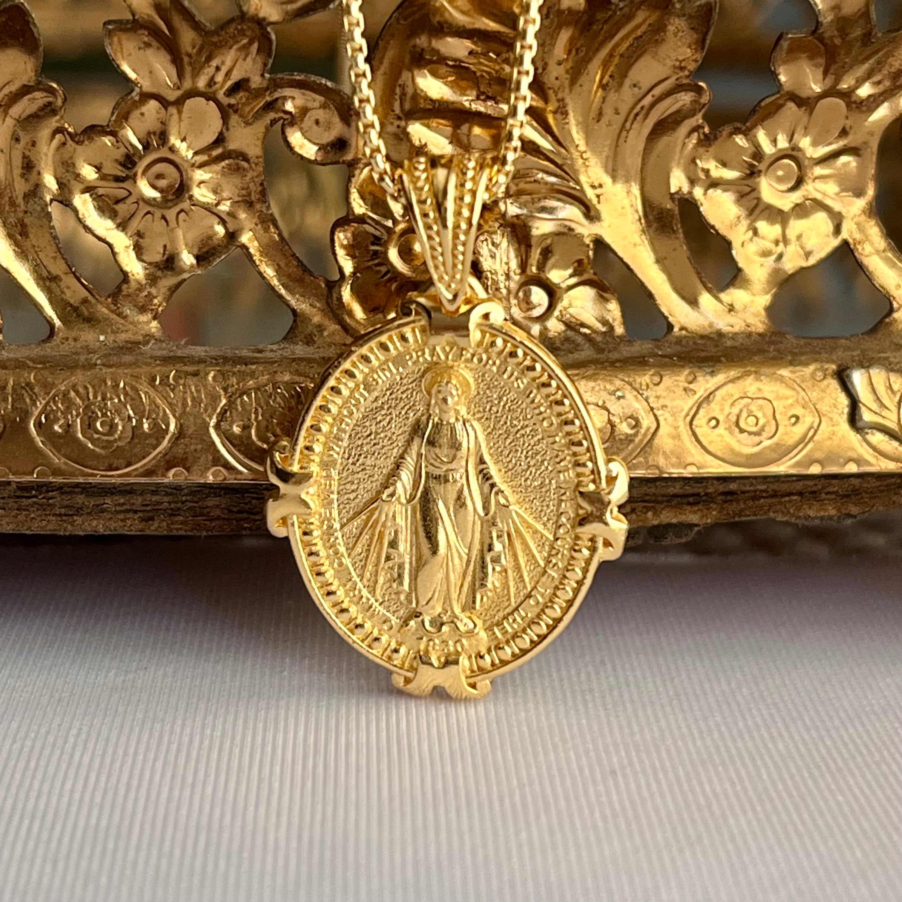 a beautiful 14 karat gold vermeil miraculous medal featuring with heavenly blue color background. The image of the Virgin Mary standing on the globe with her arm outstretched and rays of light emanating from her hands