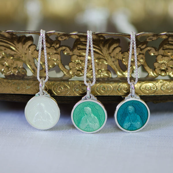 An sterling silver pendant showing the image of Our Lady of Guadalupe with an translucent enamel overlay.  Pendant is shown in three colors, white cream, light green, and teal.