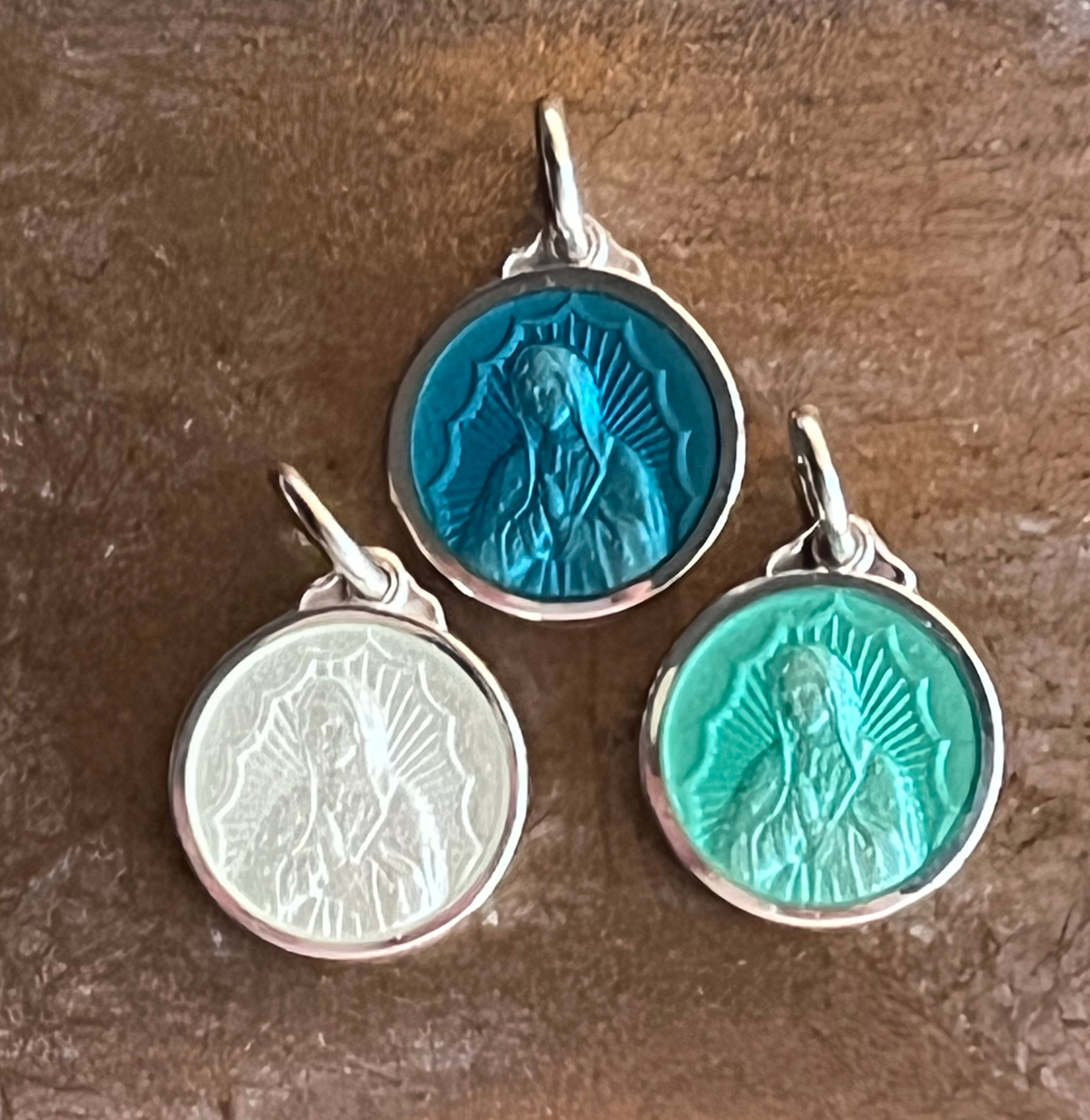 Three different color pendants featuring Our Lady of Guadalupe in enamel.  White cream, light green, and teal, shown with a sterling silver border.