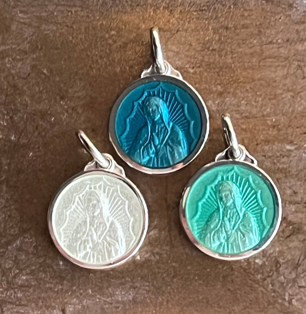Three different color pendants featuring Our Lady of Guadalupe in enamel.  White cream, light green, and teal, shown with a sterling silver border.