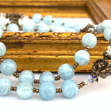 Aquamarine smoky blue rosary beads with bronze spacers and crystal beads next to rose beads.