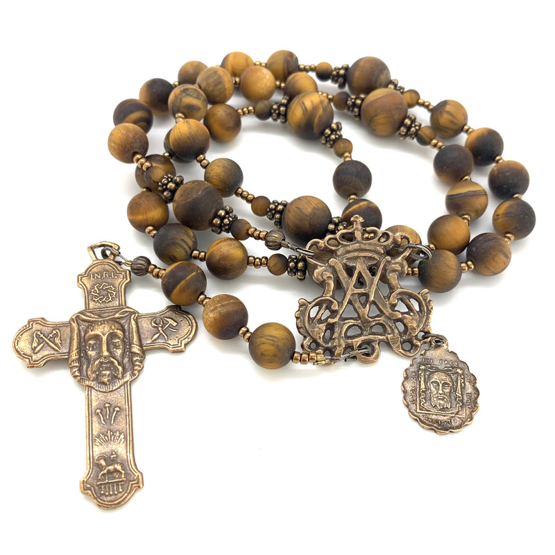 A 33 bead rosary featuring tiger eye beads, and a bronze auspice maria center along with a crucifix featuring and image of the holy face of Jesus