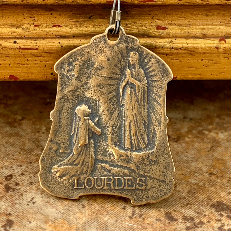 Back of Our Lady of Lourdes medal featuring Bernadette kneeling before the blessed mother.