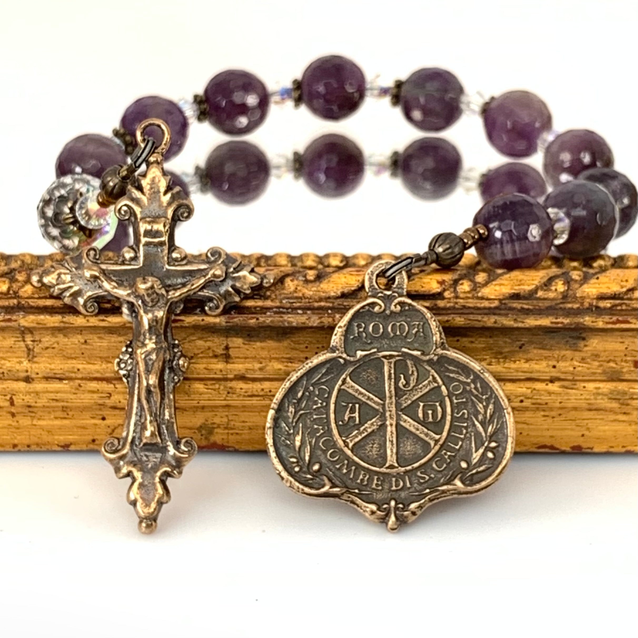 Backside of St Cecilia medal on right, crucifix on left and amethyst rosary beads in background.