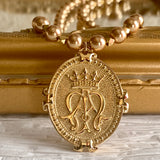 A gold vermeil pendant on pearls with the Auspice Maria logo and Mary's crown over the A and M intertwined.