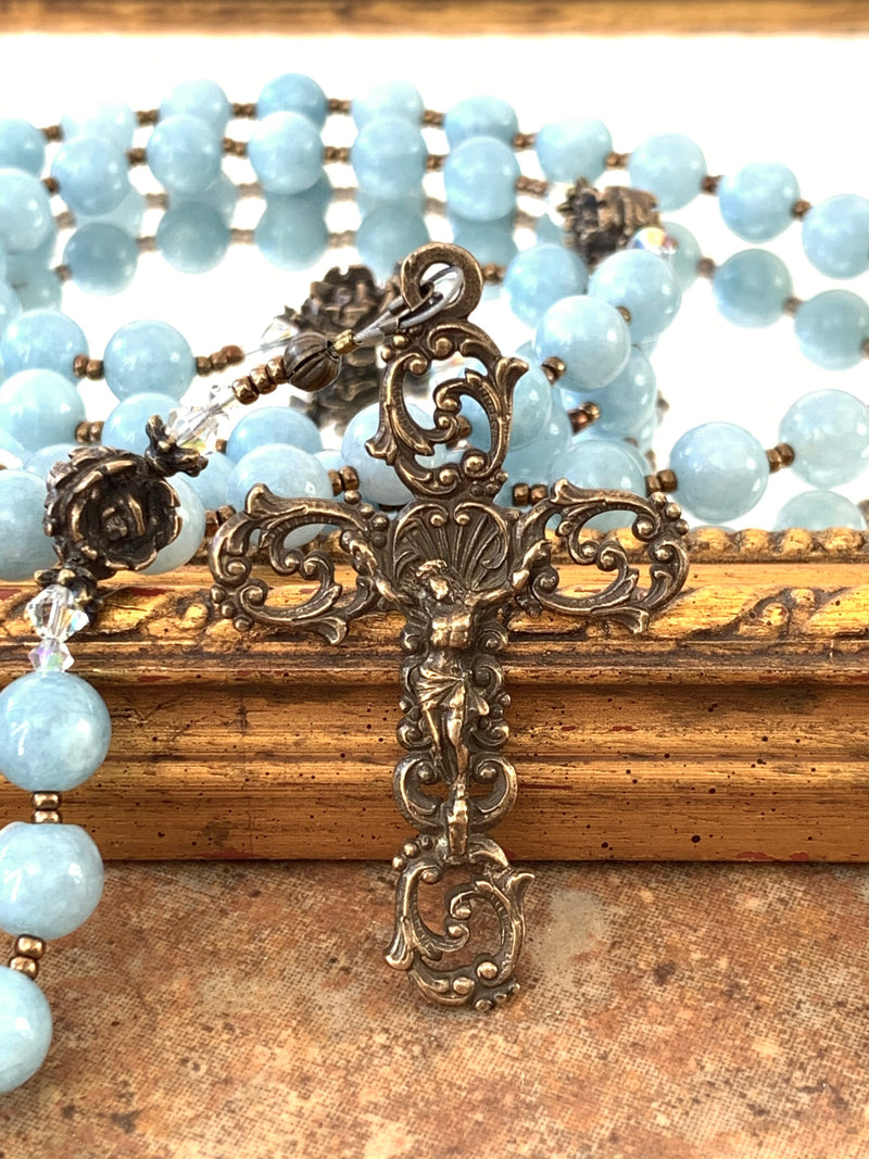 Bronze crucifix with aquamarine rosary beads in background.