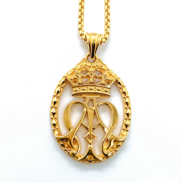 An auspice maria pendant necklace hanging on a gold chain.  Also known as an Ave Maria Necklace