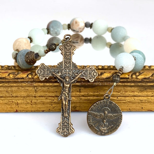 Rosary with Holy Spirit bronze medal on right, Sacred heart crucifix on left with Amazonite Ave Maria beads in background. 