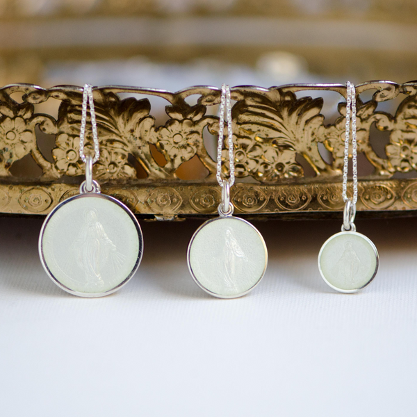 Three white enamel Miraculous medals of different sizes on silver chains.
