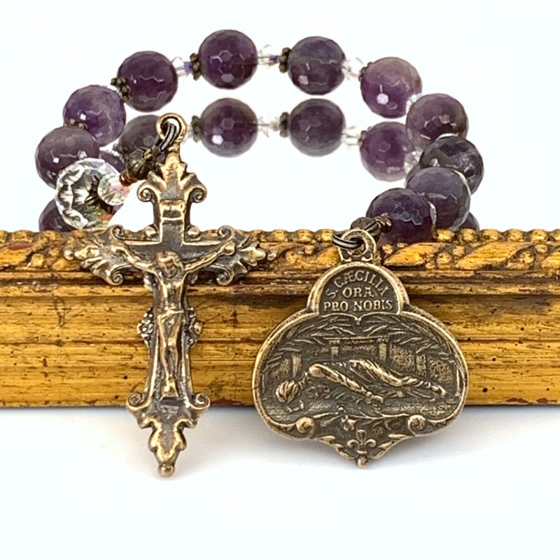 Rosary with St Cecilia Medal on right and handsome little crucifix on left with amethyst rosary beads in background.