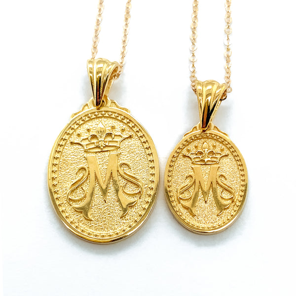 Gold Necklace pendant hanging on a gold chain.  The oval pendant features an M and a crown over the M.  The crown represents Mary's place as queen of heaven.