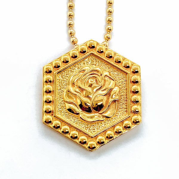 Gold hexagonal pendant hung on a bead chain.  The pendant features a rose in the center, and raised dots around the border.